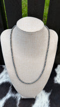A 4mm sterling silver necklace. On a linen neck bust. sitting on top of a brown and white cowhide with a brown fence background.